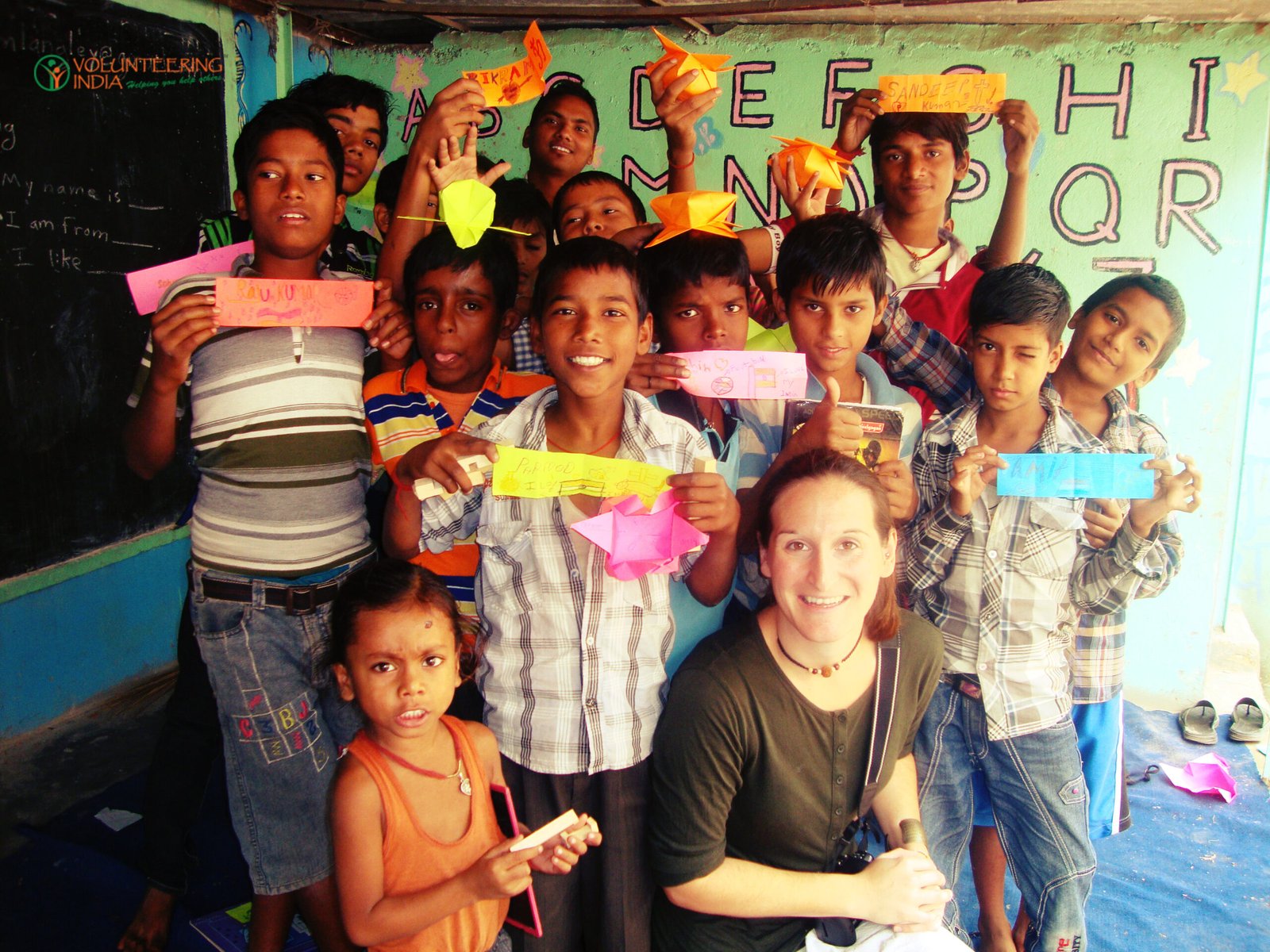 A volunteer with a group of children holding up paper crafts in a classroom