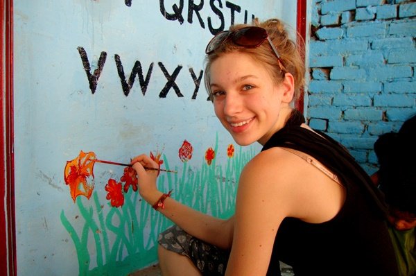 A volunteer painting flowers on a classroom wall