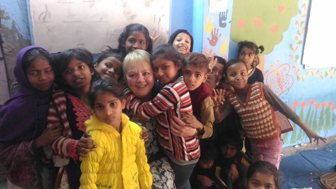An older volunteer surrounded by smiling children in a brightly painted classroom