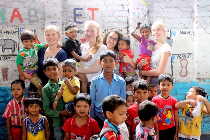 Four volunteers with a large group of children in front of an alphabet mural