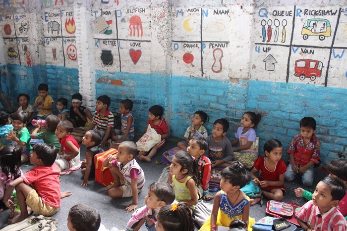 Children sitting on the classroom floor at a center in Delhi, below a wall painted with letters and pictures
