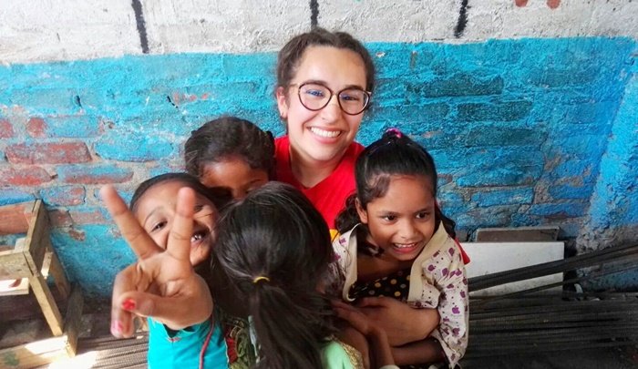 A smiling volunteer hugging a group of girls, one of them making a peace sign