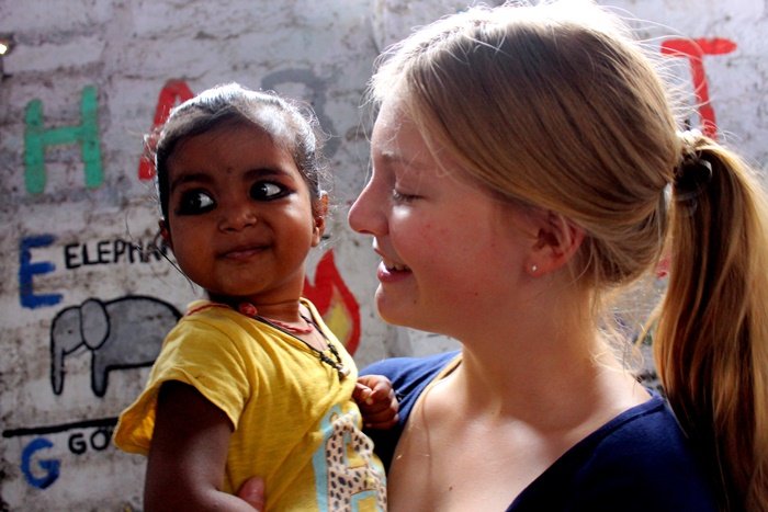 A volunteer smiling at a toddler in her arms, in front of a wall painted with the alphabet