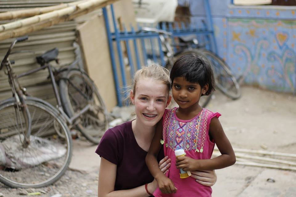 A volunteer kneeling beside a young girl in a lane lined with bicycles