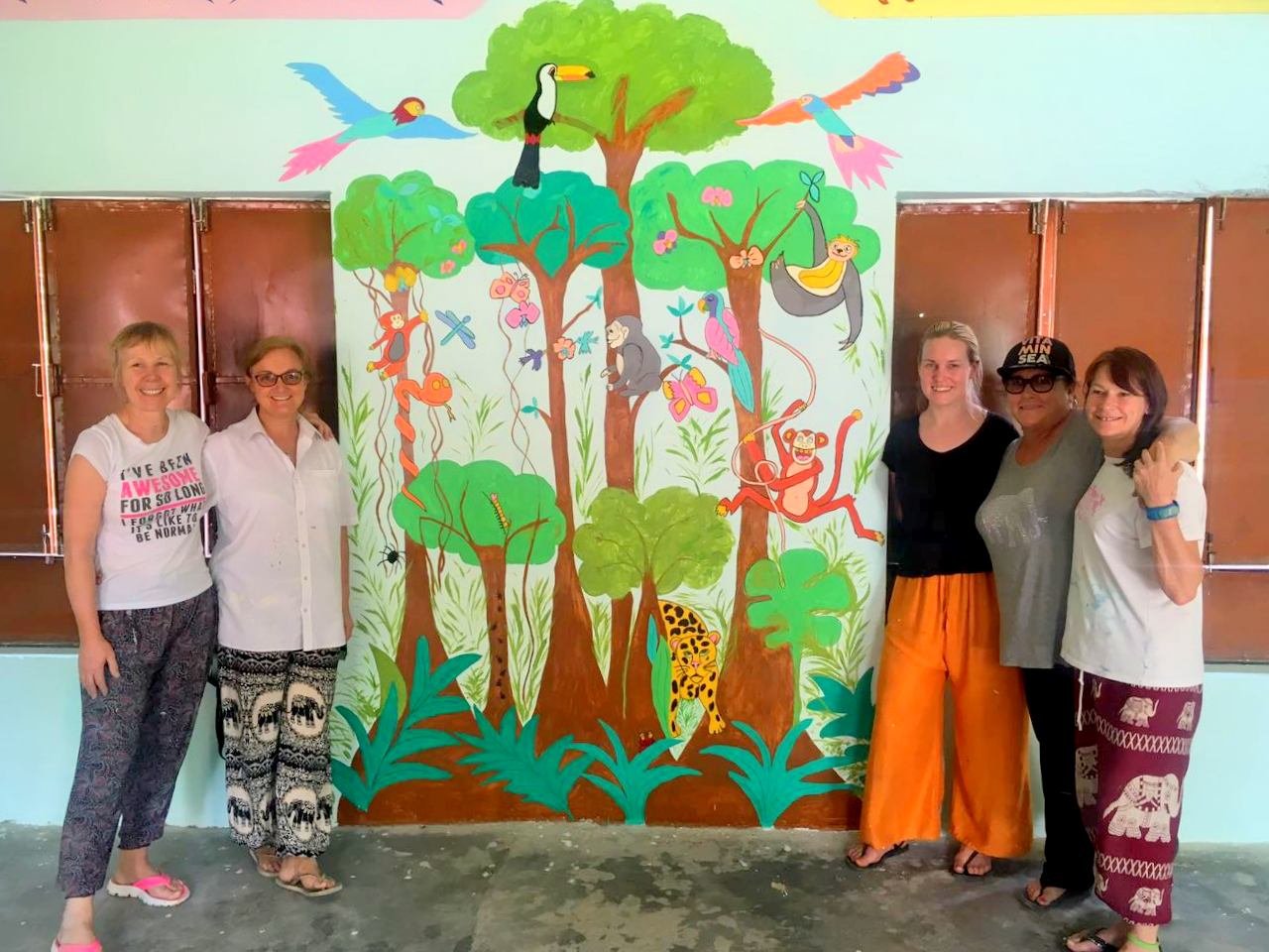 Five volunteers on either side of a jungle mural on a classroom wall