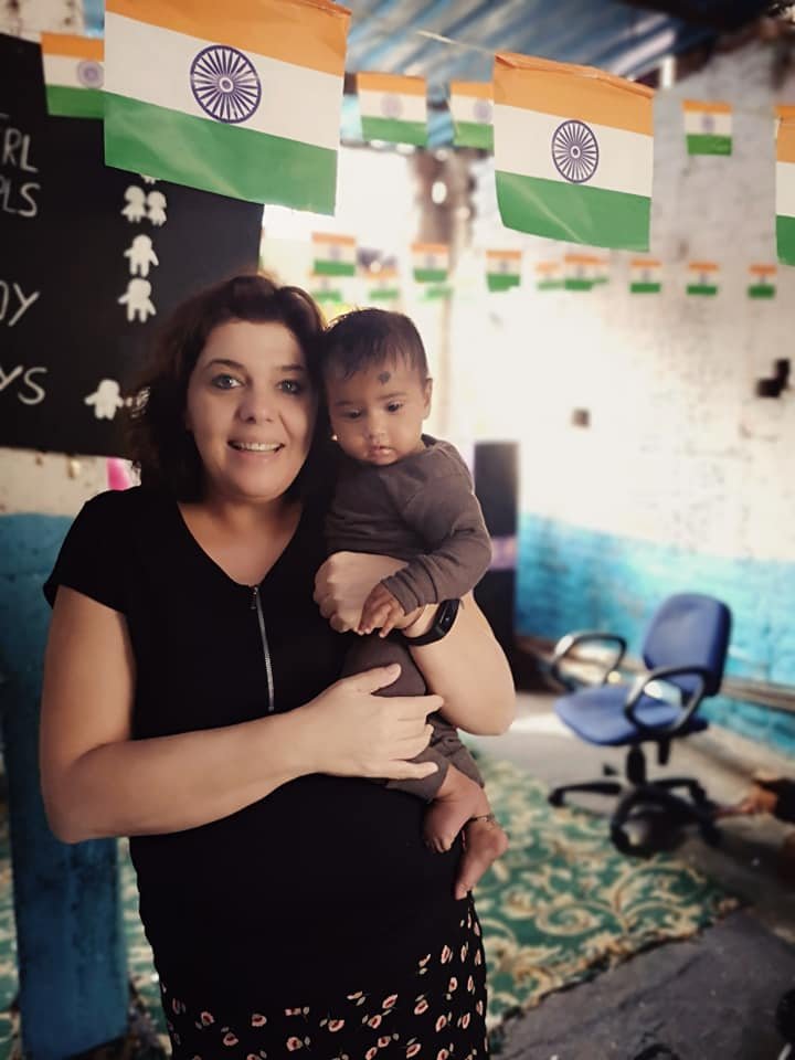 Daphne holding a toddler in a classroom decorated with Indian flags