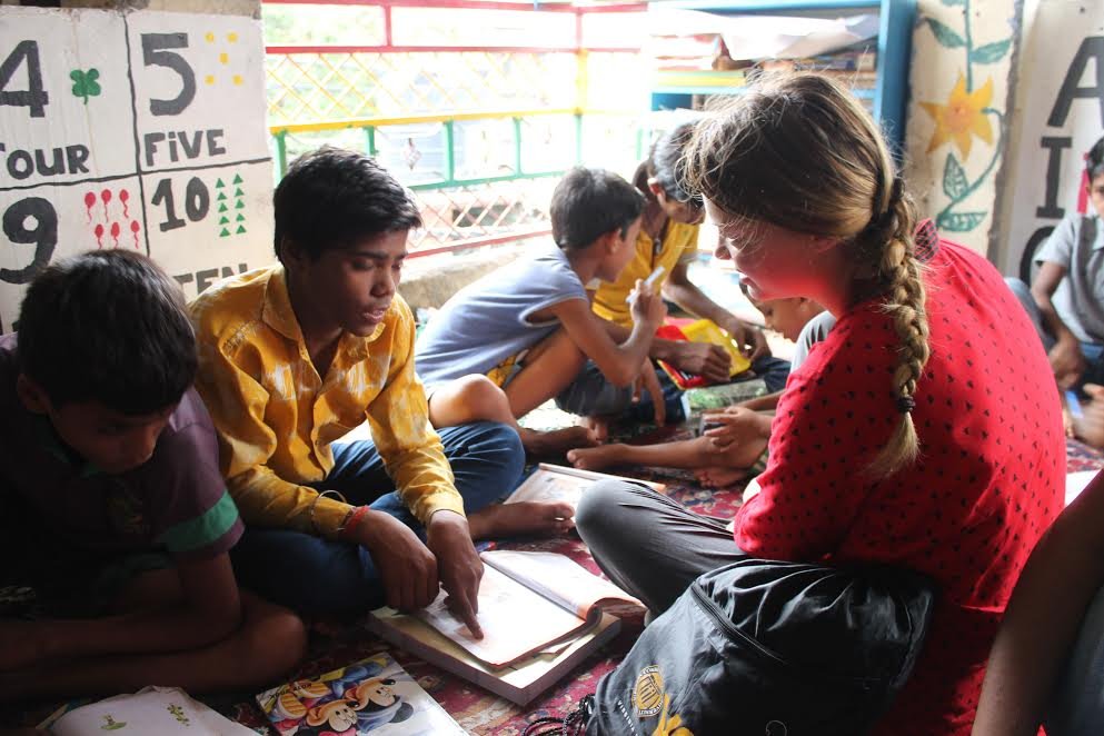 A volunteer sitting on the floor with a group of boys, helping them with their schoolwork