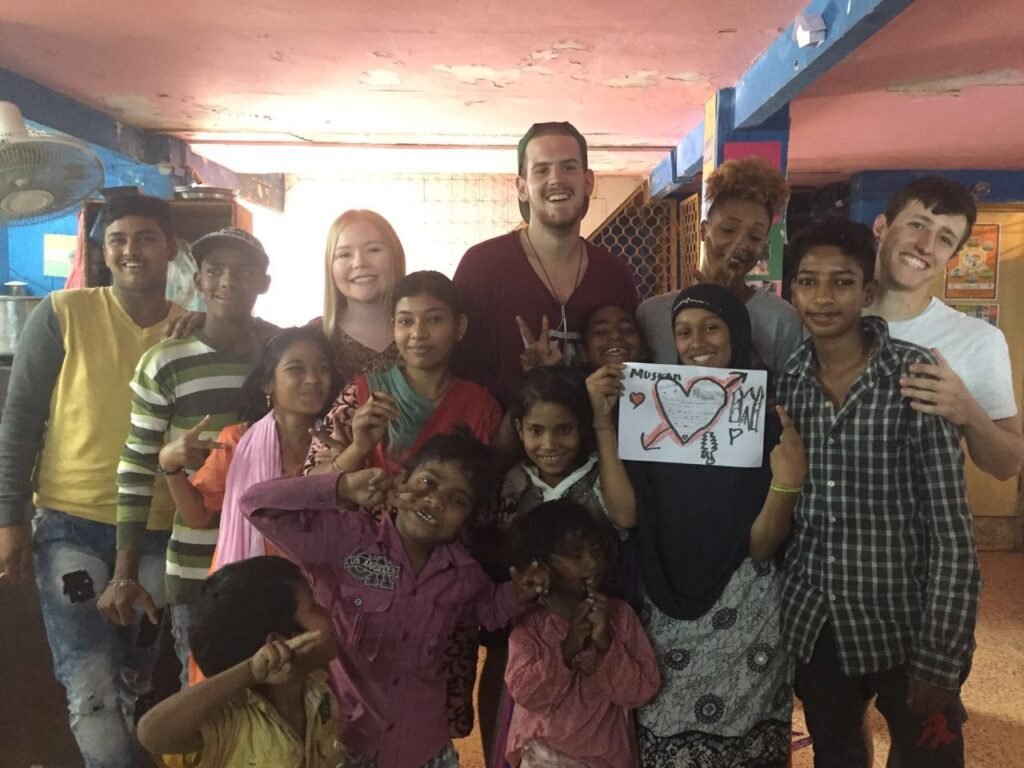 Volunteers and children together at a children’s center, one girl holding up a drawing
