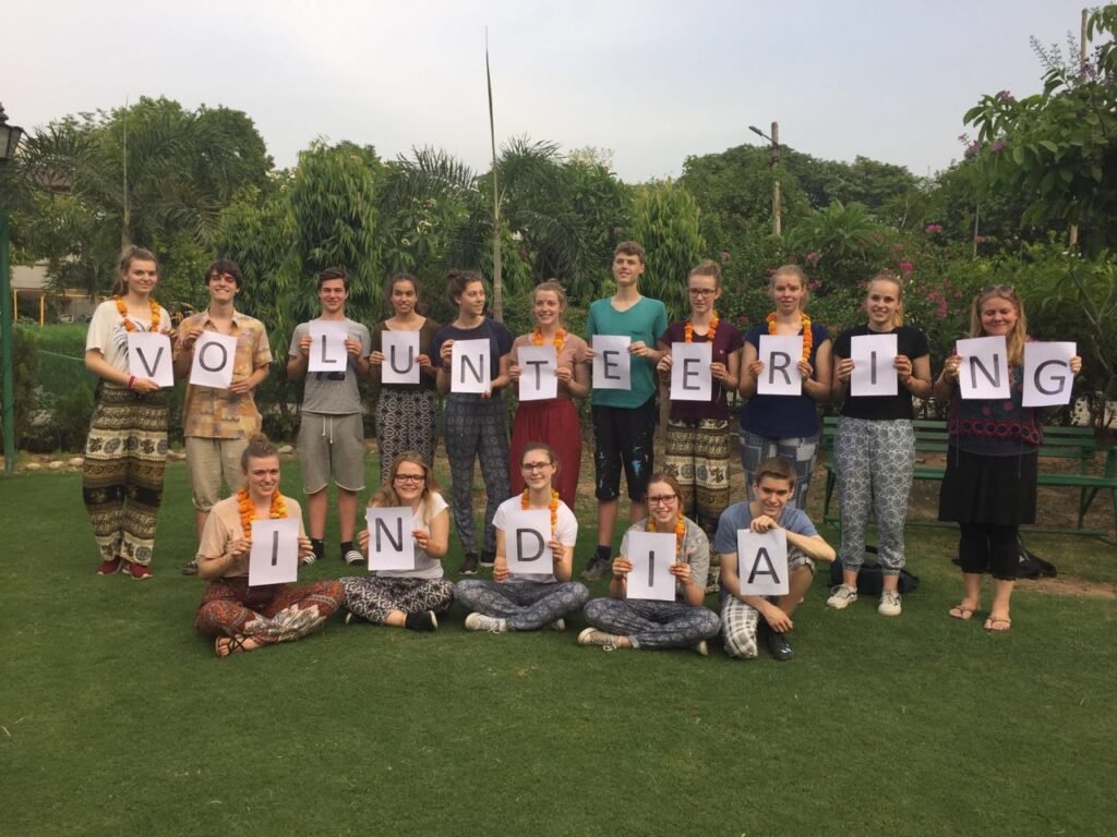 Volunteers in marigold garlands holding up letters that spell Volunteering India