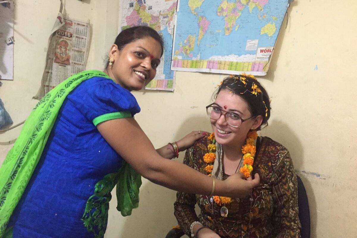A teacher placing a marigold garland on a new volunteer in Delhi