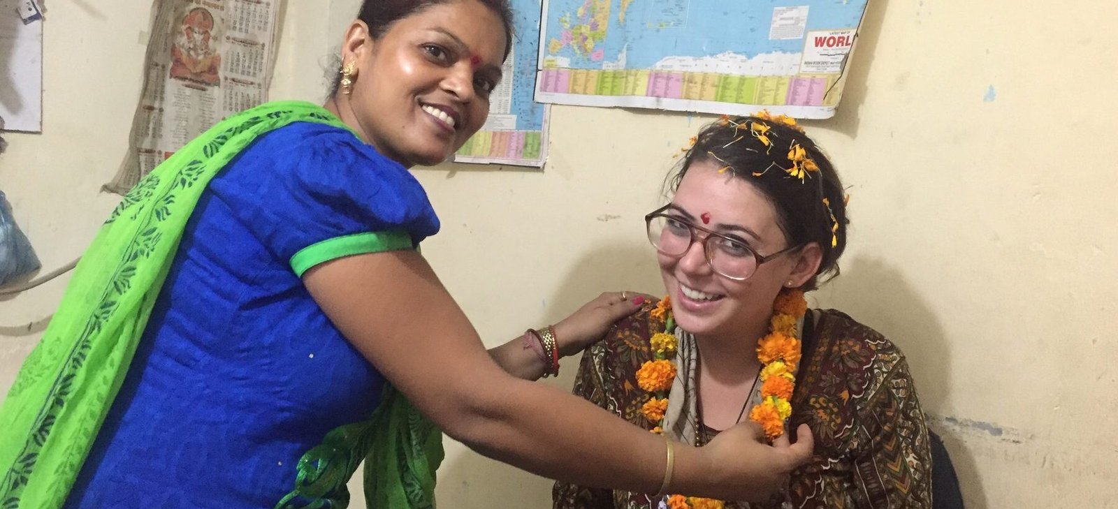 A teacher placing a marigold garland on a new volunteer in Delhi
