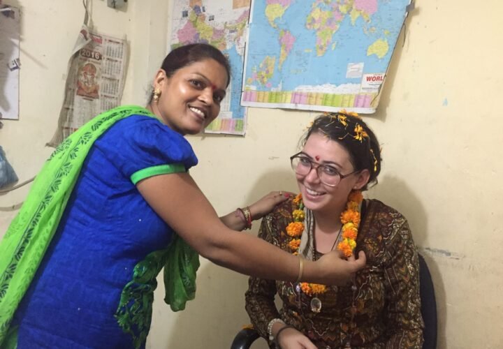 A teacher placing a marigold garland on a new volunteer in Delhi