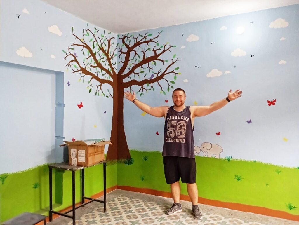 A volunteer in a room he helped paint with a tree and rainbow mural in Jaipur