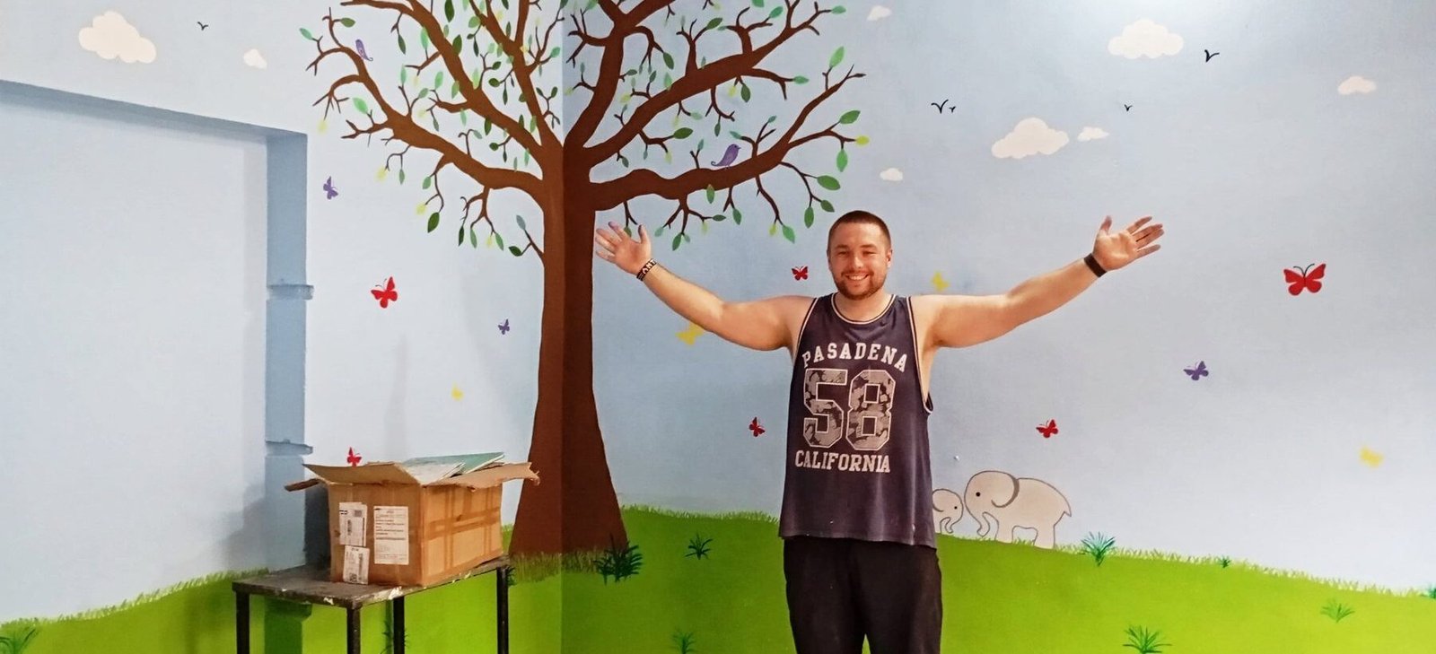A volunteer in a room he helped paint with a tree and rainbow mural in Jaipur
