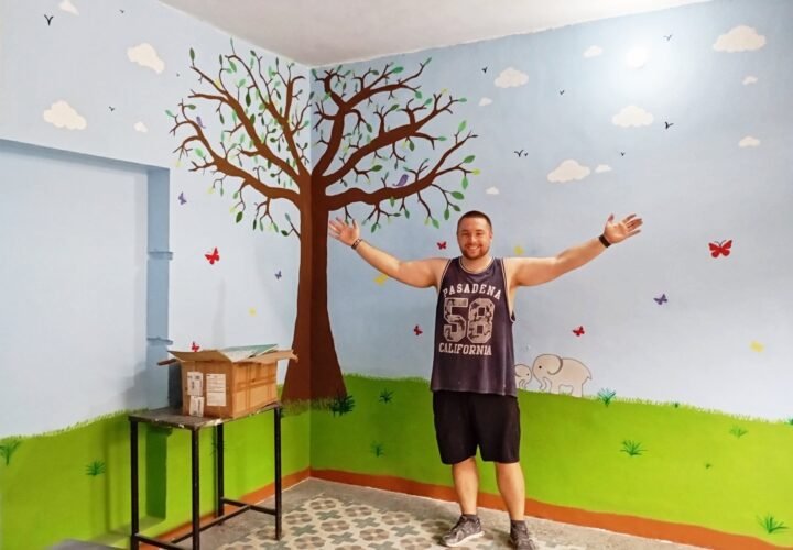 A volunteer in a room he helped paint with a tree and rainbow mural in Jaipur