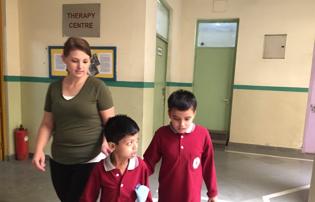 A volunteer walking with two students along a corridor at a special needs center in Delhi