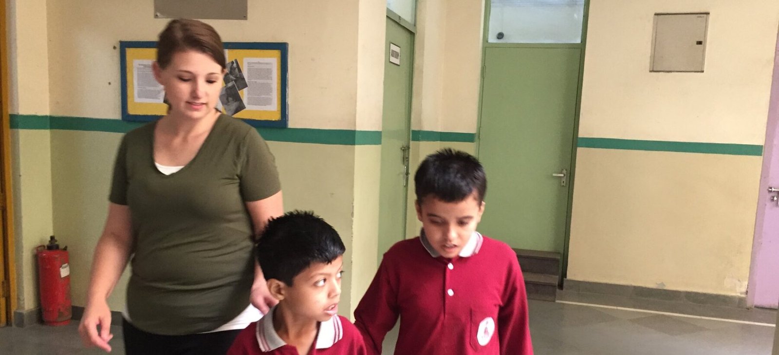 A volunteer walking with two students along a corridor at a special needs center in Delhi