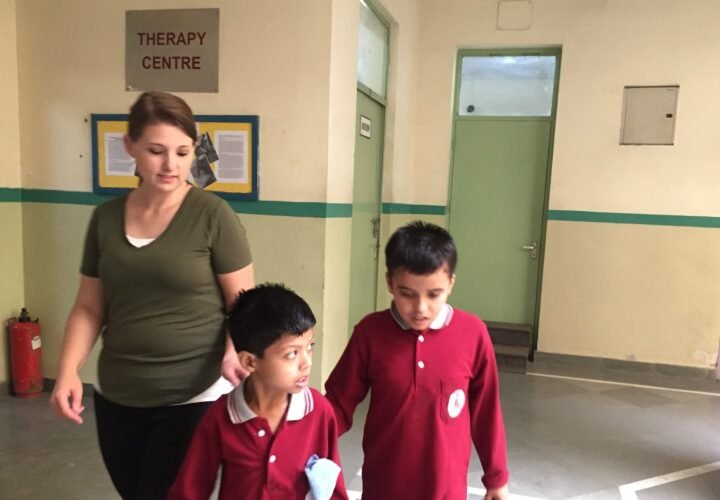 A volunteer walking with two students along a corridor at a special needs center in Delhi