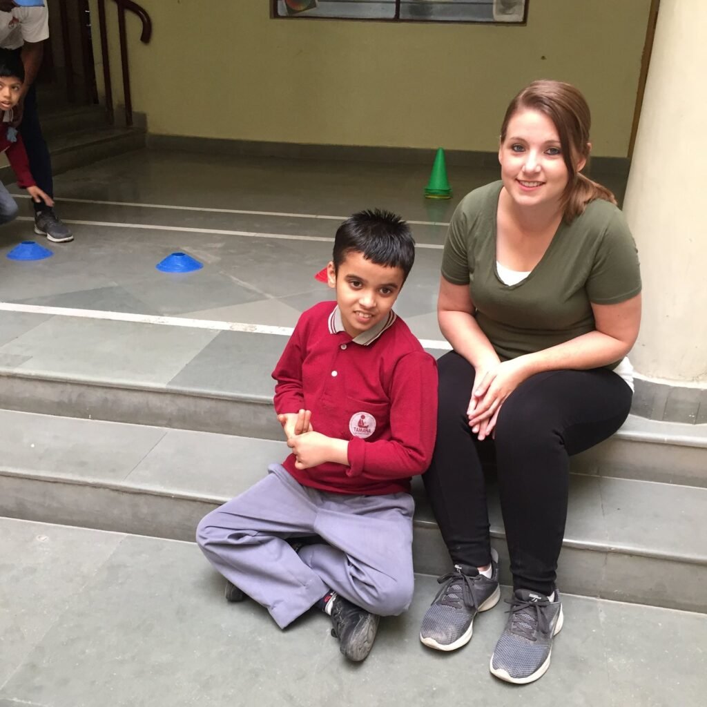 A volunteer sitting on the steps with a student at a special needs center in Delhi