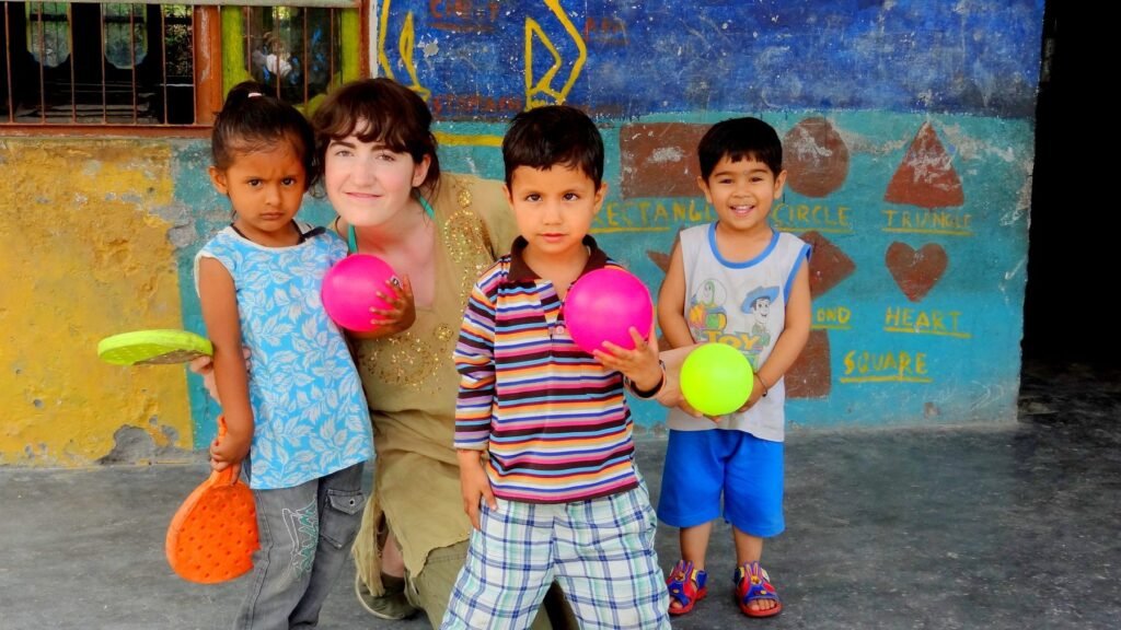 A volunteer playing with young children holding balls and bats at a project in Delhi
