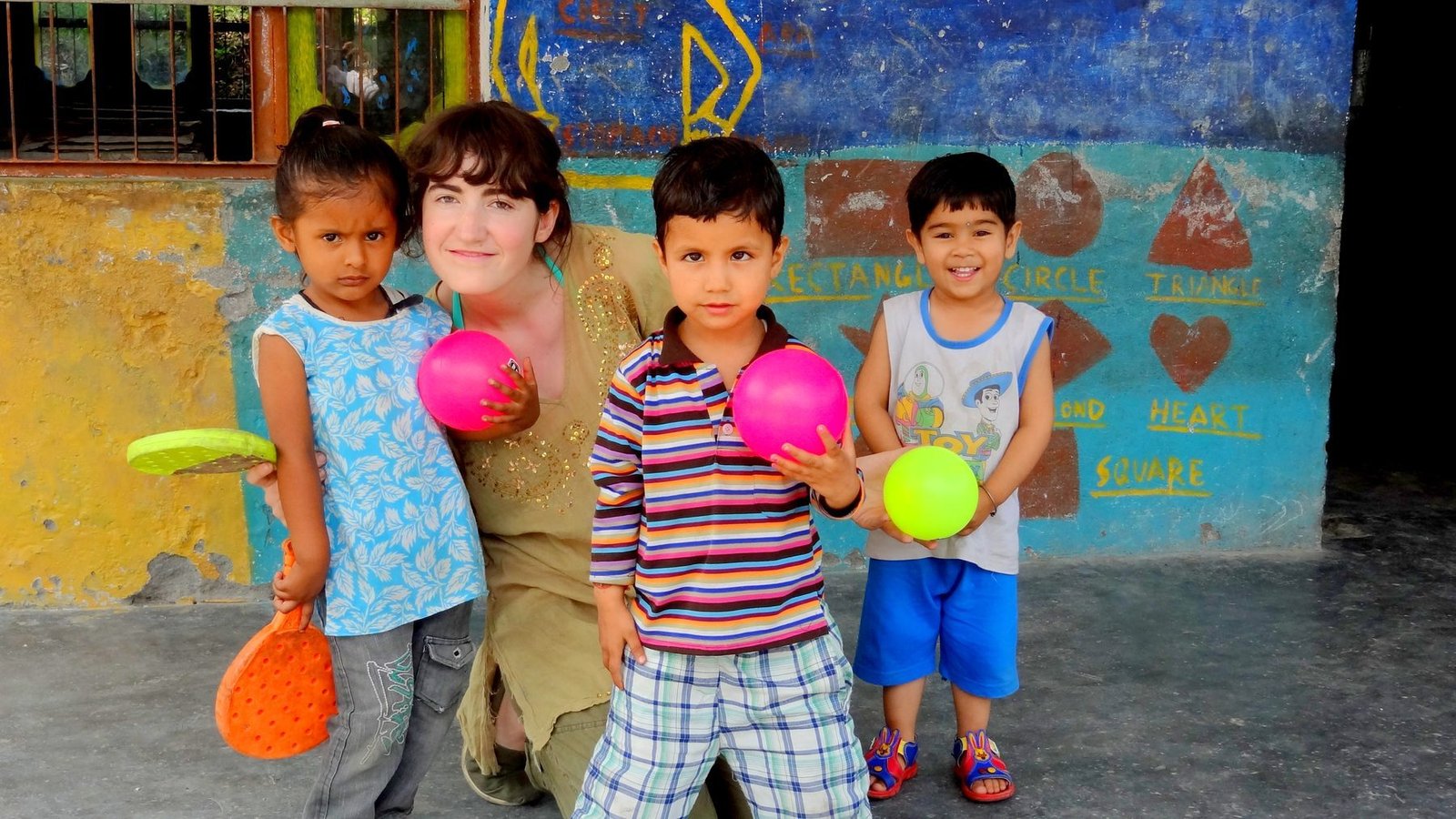 A volunteer playing with young children holding balls and bats at a project in Delhi