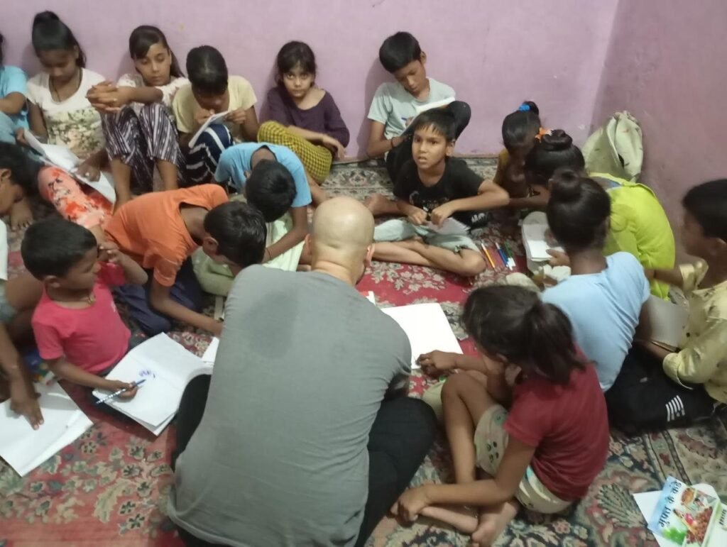 A volunteer helping children with schoolwork on the floor of a center in Jaipur