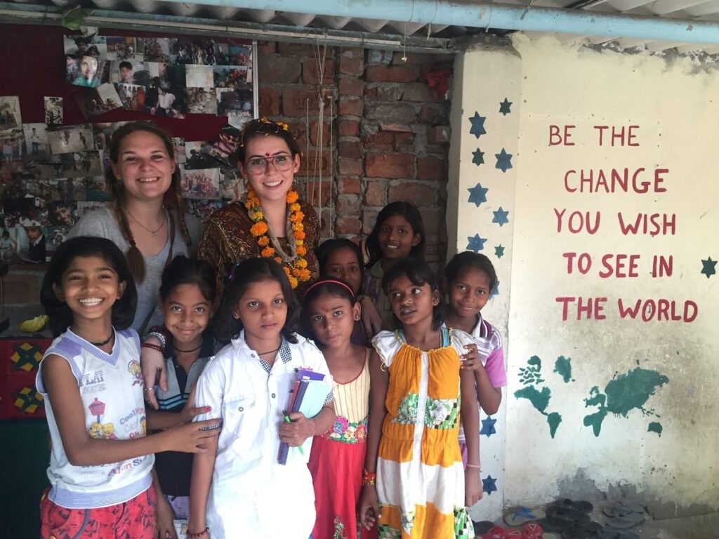 Two volunteers with girls at a children’s center in Delhi, beside a wall painted with “Be the change you wish to see in the world”