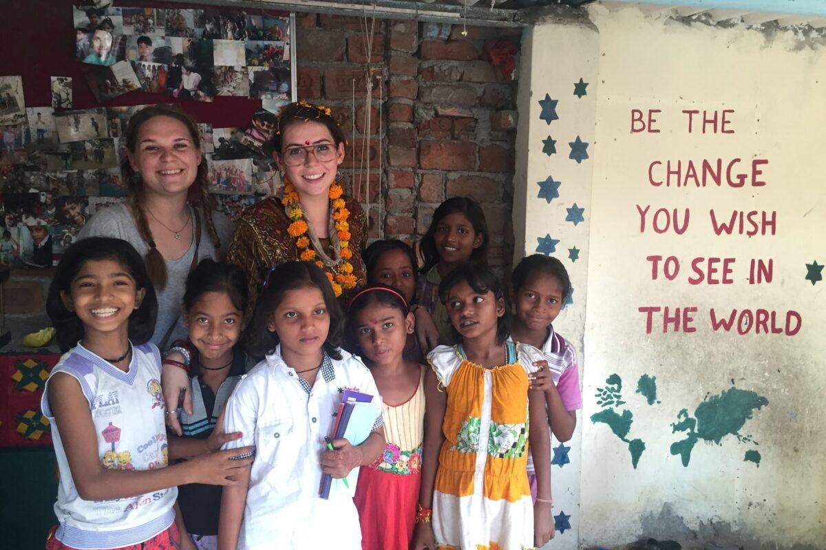 Two volunteers with girls at a children’s center in Delhi, beside a wall painted with “Be the change you wish to see in the world”