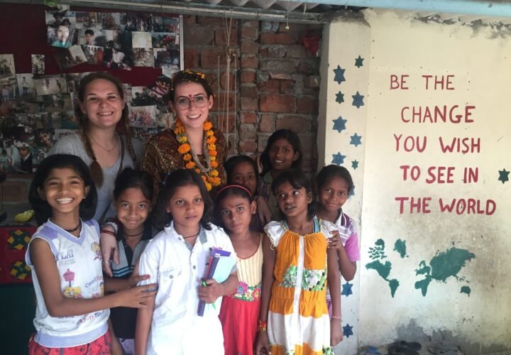 Two volunteers with girls at a children’s center in Delhi, beside a wall painted with “Be the change you wish to see in the world”